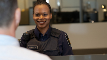 Employée en uniforme derrière un comptoir de service, faisant face à une personne visiteuse 