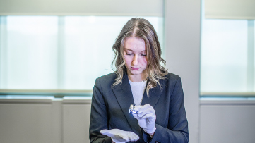 Femme portant un veston foncé qui examine un petit objet dans un bureau avec des fenêtres givrées.